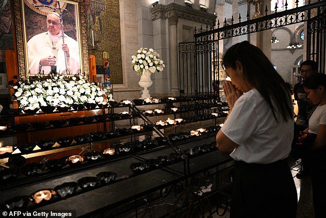 A woman offer prayers in front of a portrait of Pope Francis prior to a requiem mass at the Manila Cathedra in Manila on April 22, 2025