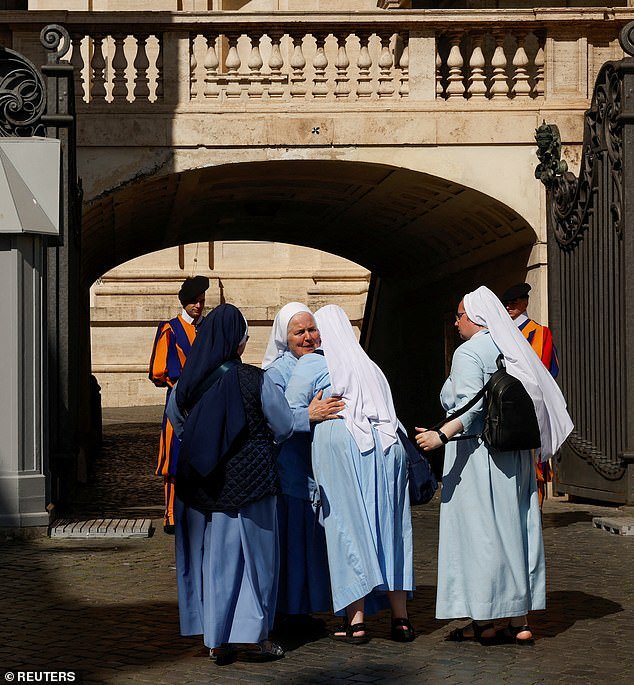 Nuns embrace each other at the Vatican, with the Swiss Guards standing guard, today as they mourn the death of the Holy Father