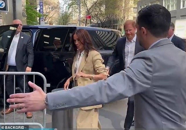 Moments later, the mother-of-two was so busy waving to crowds as she entered the building that, when Harry reached out to her once more, he was again left trailing behind
