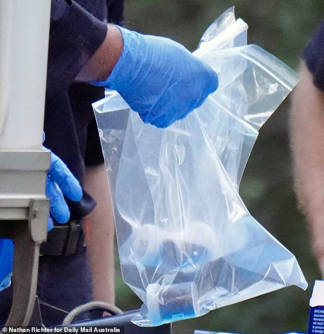 An officer is pictured carrying one of several plastic bags with sample jars full of soil
