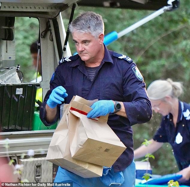 An officer is pictured carrying brown paper evidence bags at Good Night Scrub Park on Saturday as investigations into the missing 17-year-old continue
