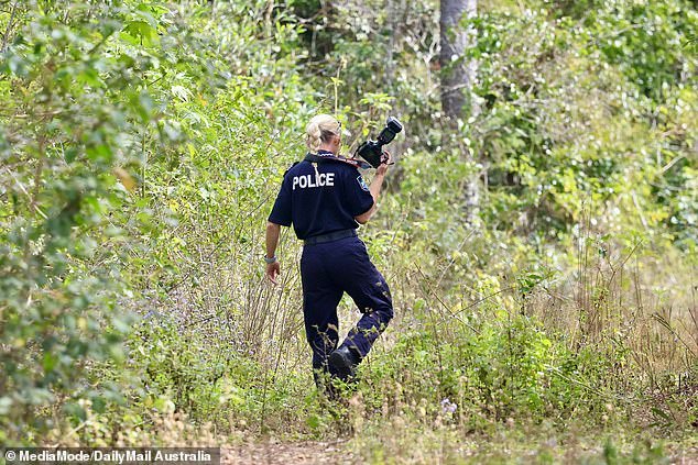 A forensic officer is seen entering the dense bushland armed with a camera