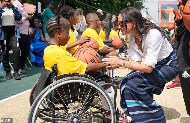 Meghan holds hands with a girl on a wheelchair during the couple's visit to Lagos yesterday