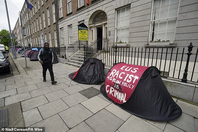 People walking past tents housing asylum seekers near to the European Parliament Liaison Office